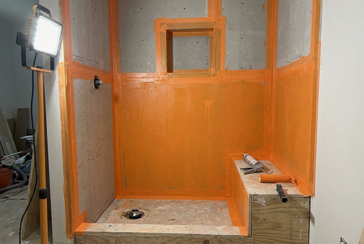 Orange waterproofing membrane coats a framed shower pan